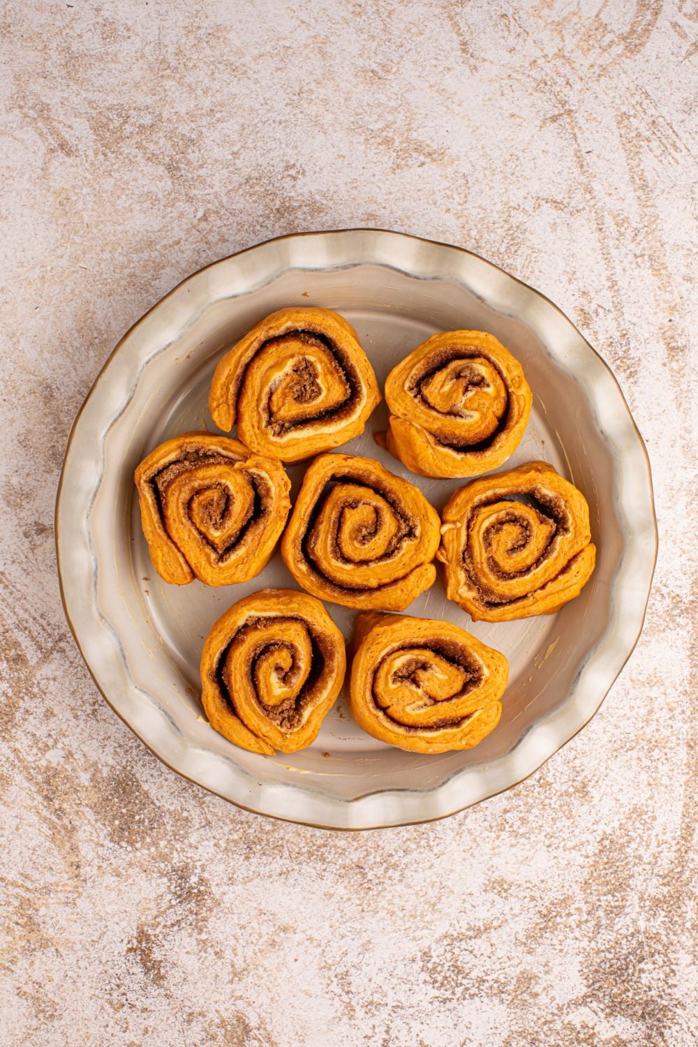 raw Pumpkin Cinnamon Rolls in a pie plate on counter 