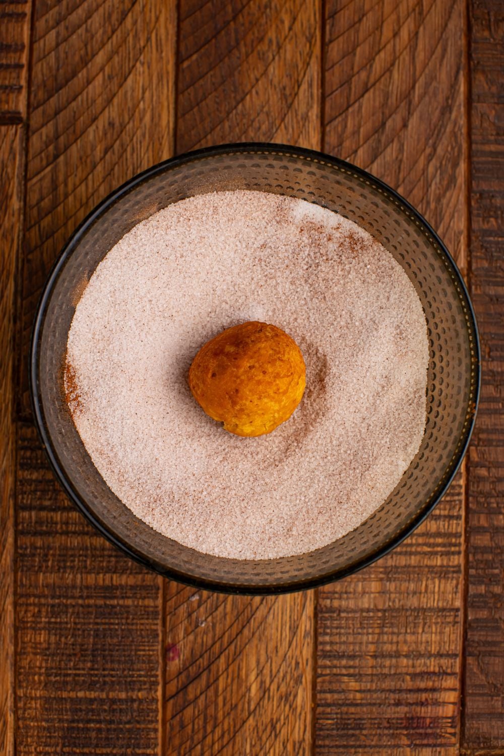 cinnamon sugar mixture in a glass bowl with a donut hole in center of the bowl on a wooden table