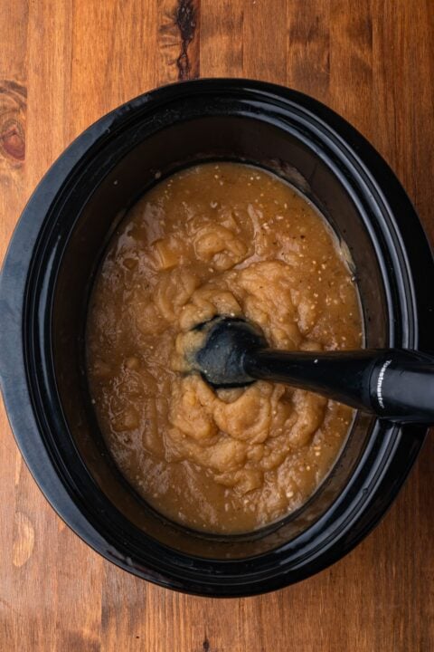 immersion blender in a black crockpot on wooden table mixing up the potato soup to make it thicker and creamy