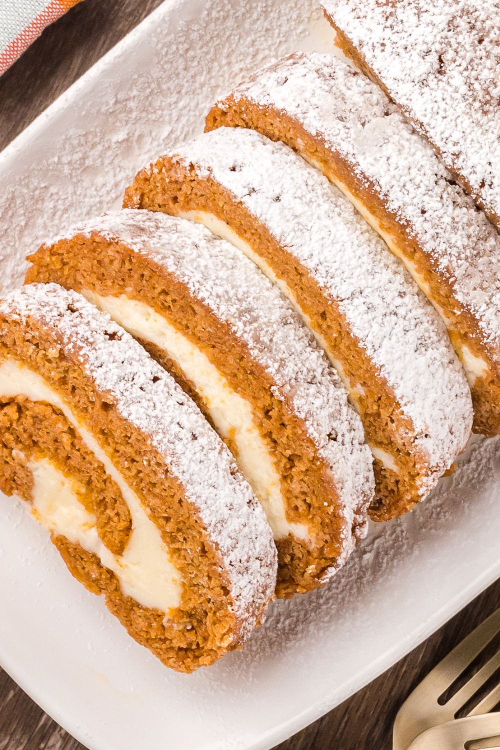 sliced Pumpkin Cake Roll on a tray sitting on a wooden table with a fork to the side