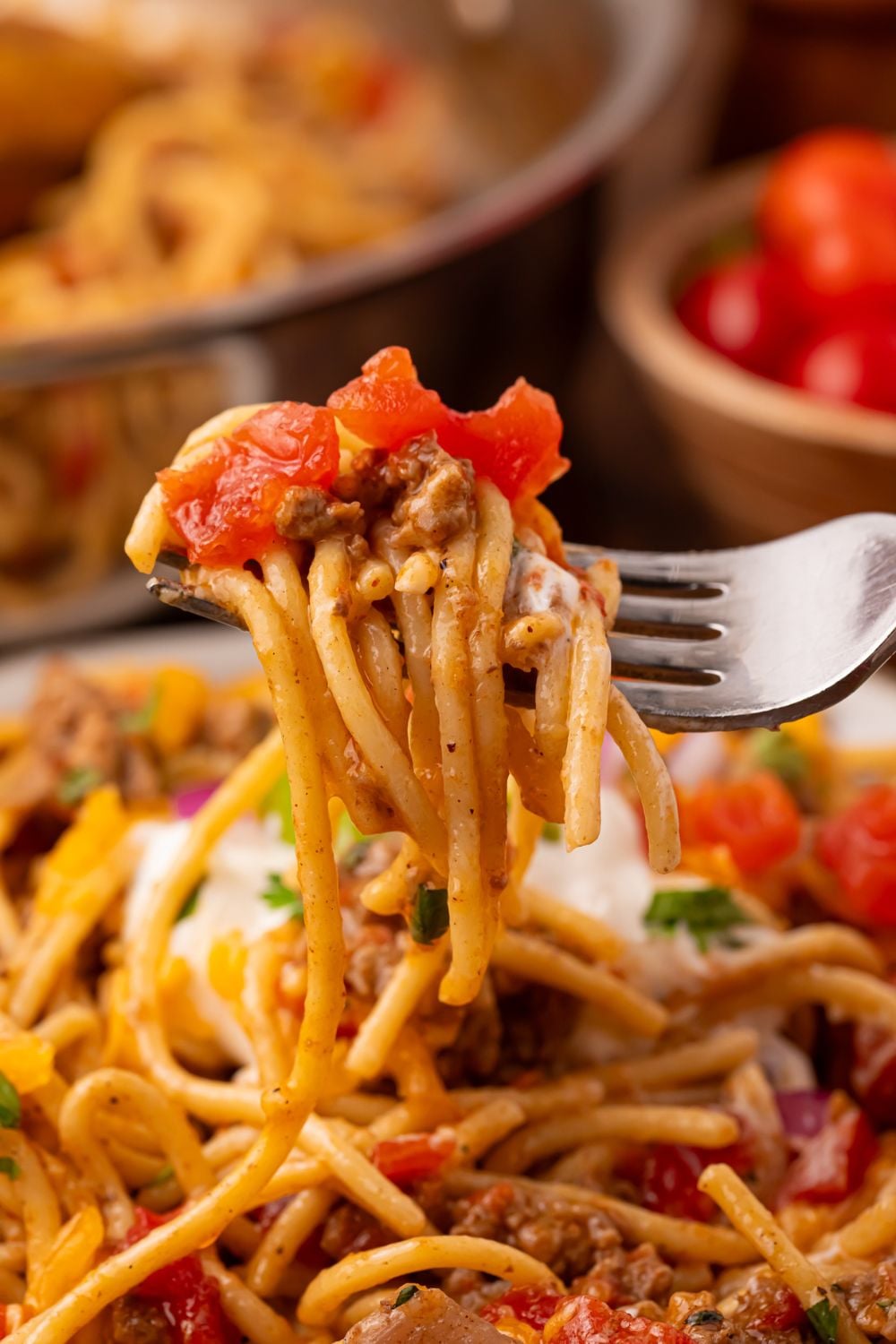 a plate with Cheesy Taco Spaghetti on it, and a fork full of pasta being lifting up off the plate