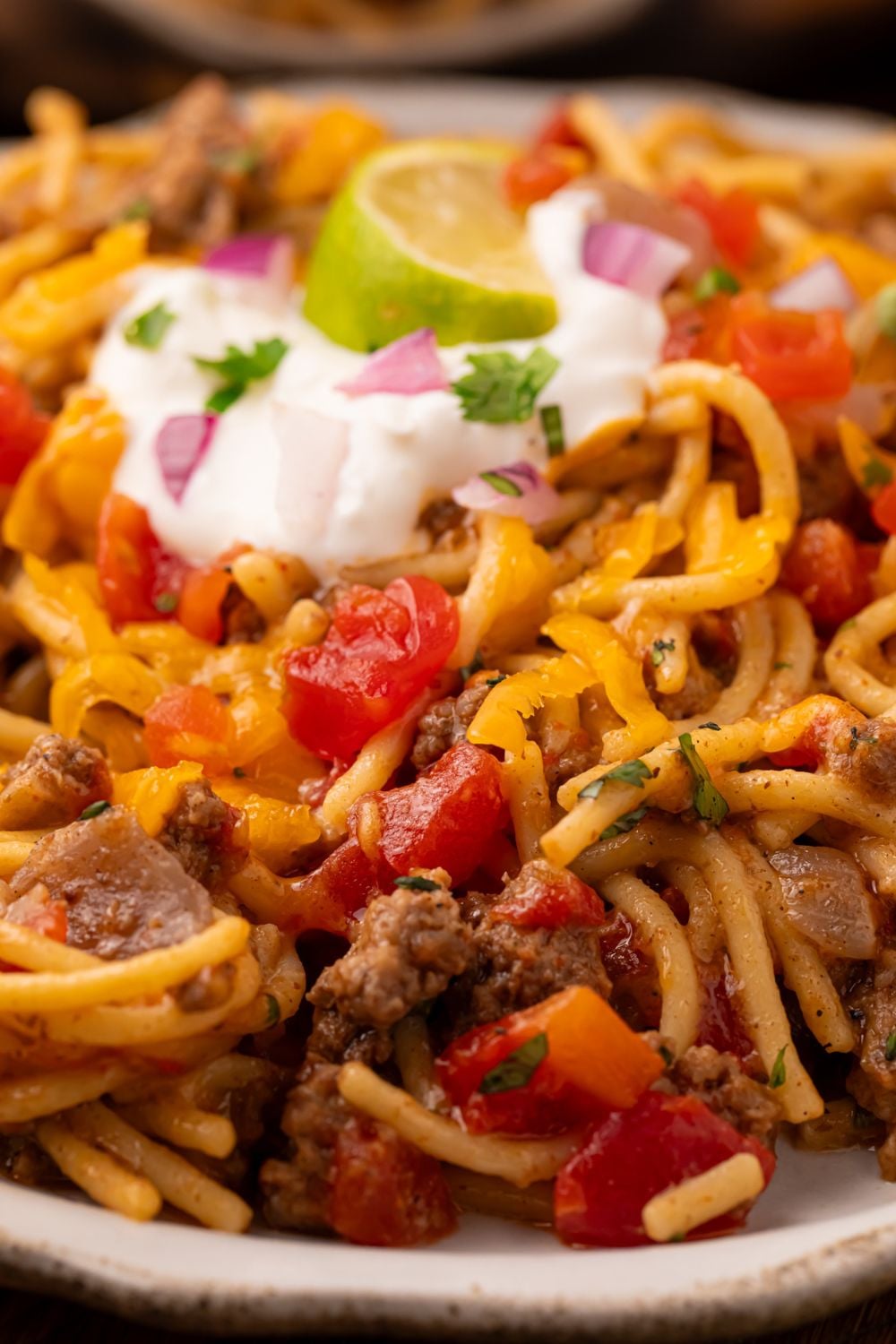 Taco spaghetti skillet on a white plate with a dollop of sour cream in center, cilantro, and a lime wedge