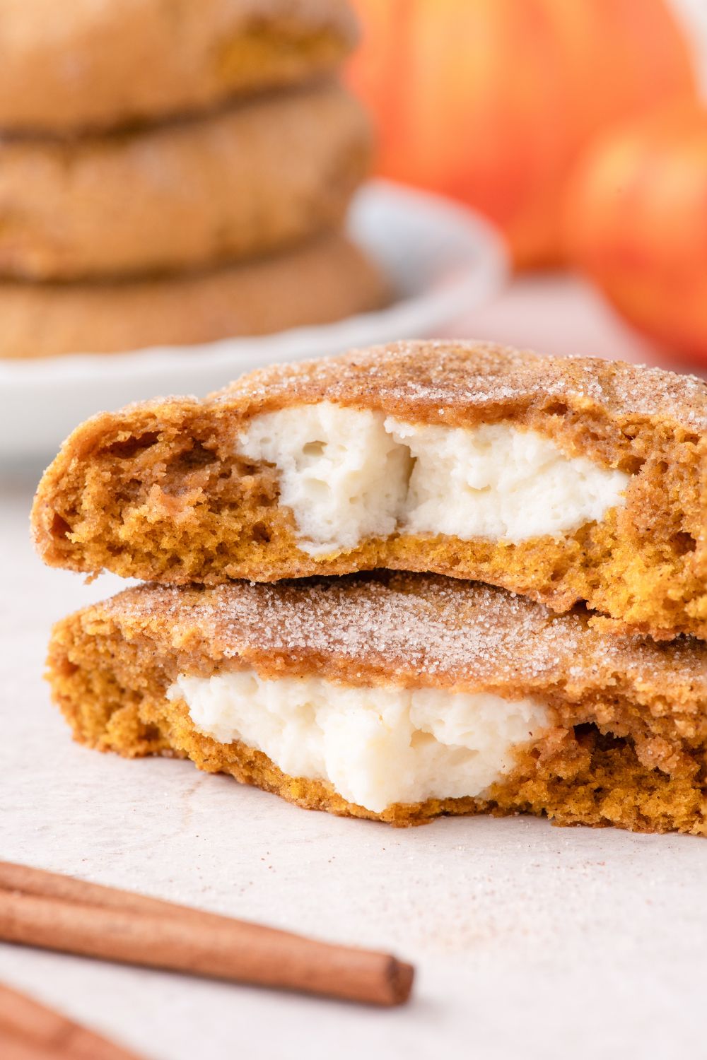 white table with two pumpkin cheesecake cookies on it, with a cinnamon stick placed in frotn