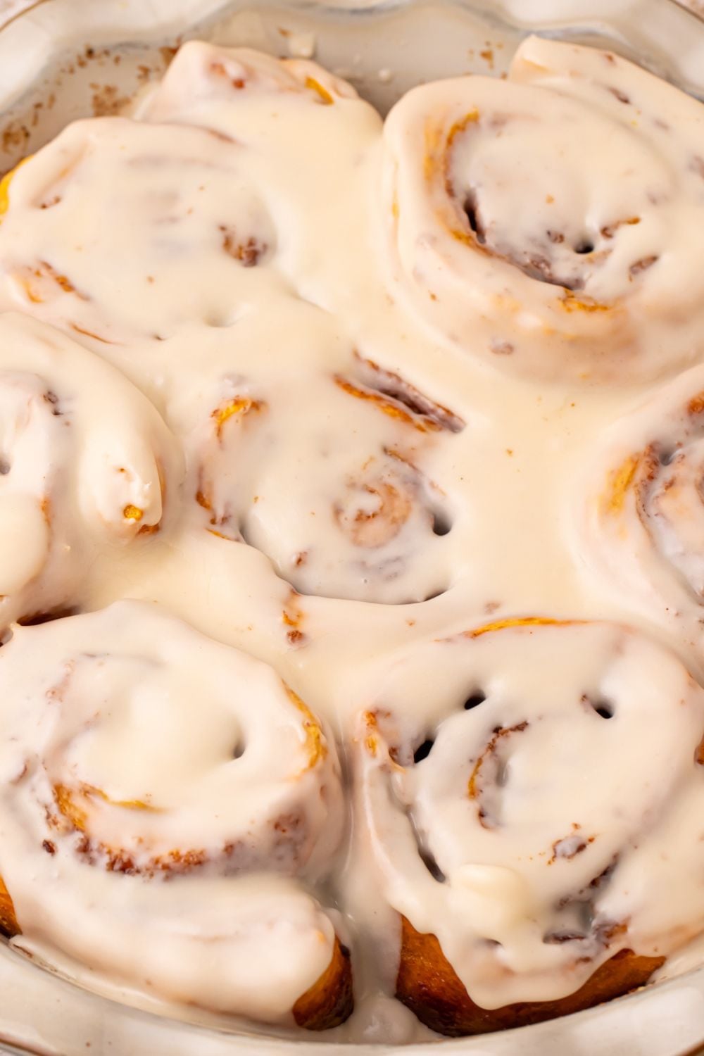 view of a close up of Pumpkin Cinnamon Rolls in a pan on table. You can see all the glaze seeped into the rolls 