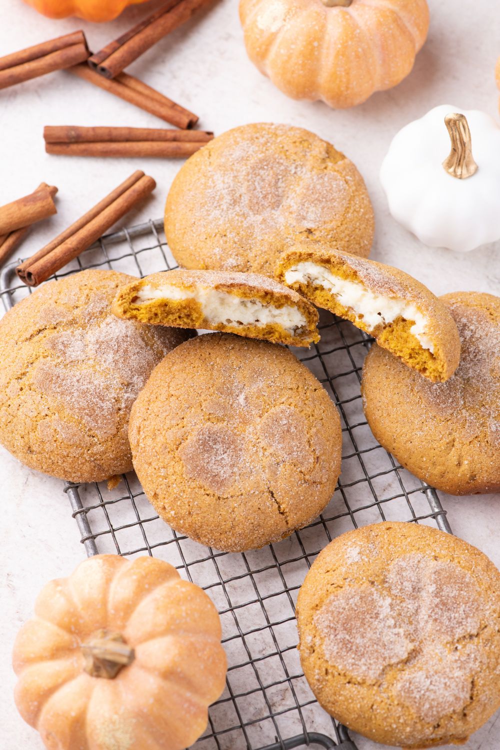 Pumpkin Cheesecake Cookies on a cooling rack on a white table with cinnamon sticks and pumpkins around