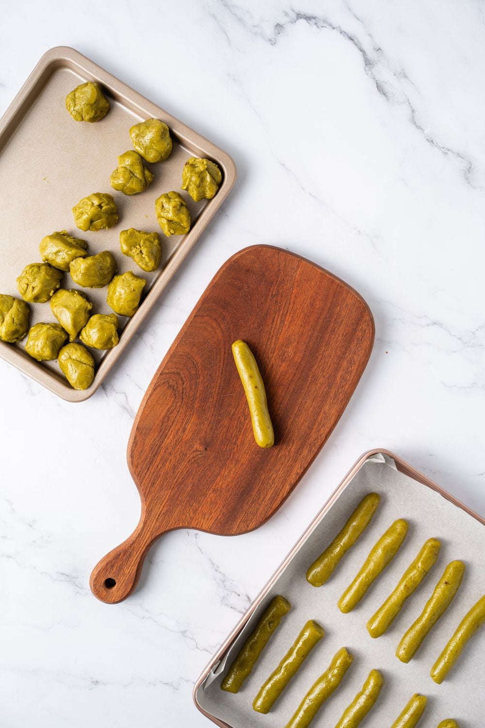 Witch Finger Cookie dough on a tray with a wooden tray with a shape of fingers and another tray with balls of cookie dough