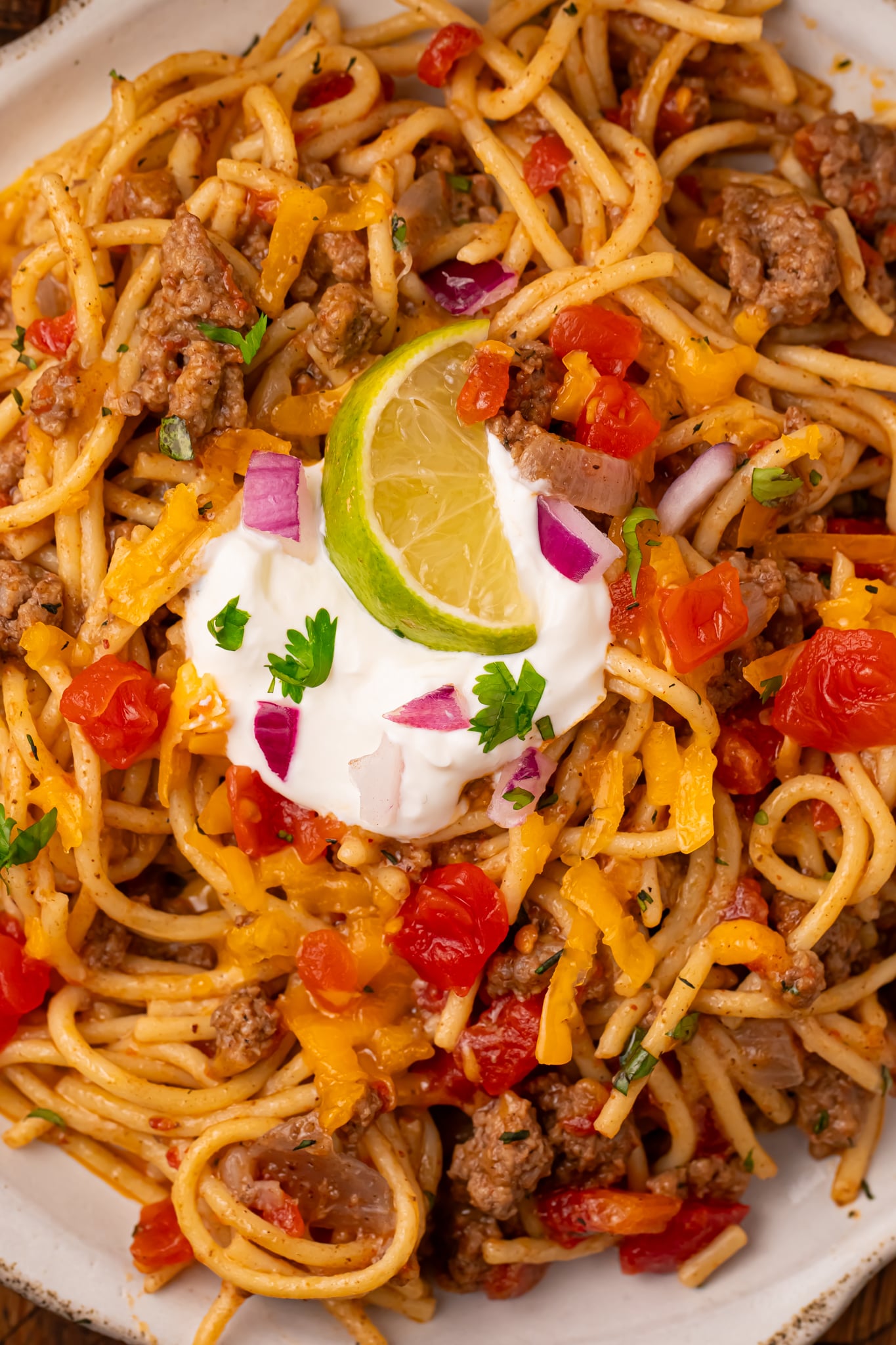 Plate of Cheesy Taco Spaghetti topped with sour cream and lime