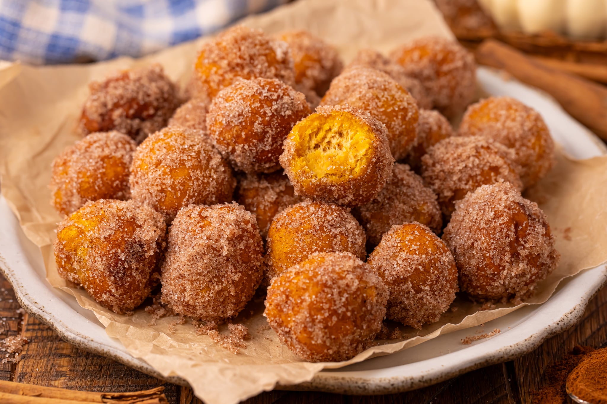 Pumpkin Pie Donut Holes scattered on a parchment lined white platter on a wooden table.