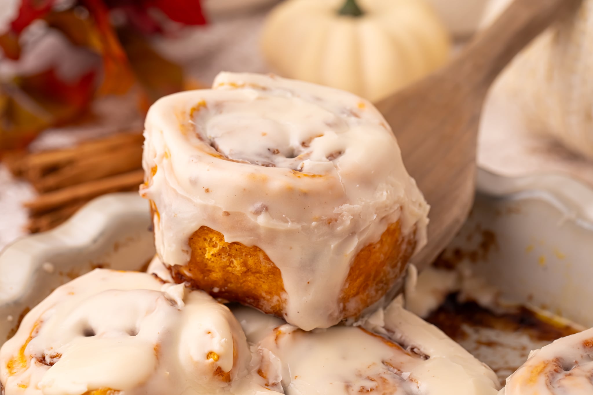 Easy 2 Ingredient Pumpkin Cinnamon Rolls in a baking dish smothered in icing with one being lifted up 