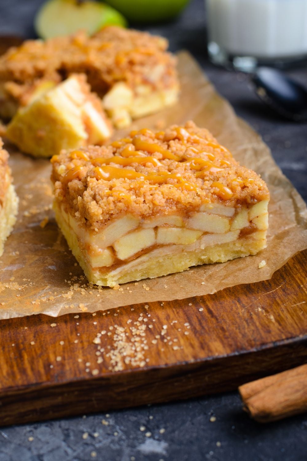 Caramel Apple Pie Bar on wooden cutting board showing the layers of apples with a cinnamon stick in front