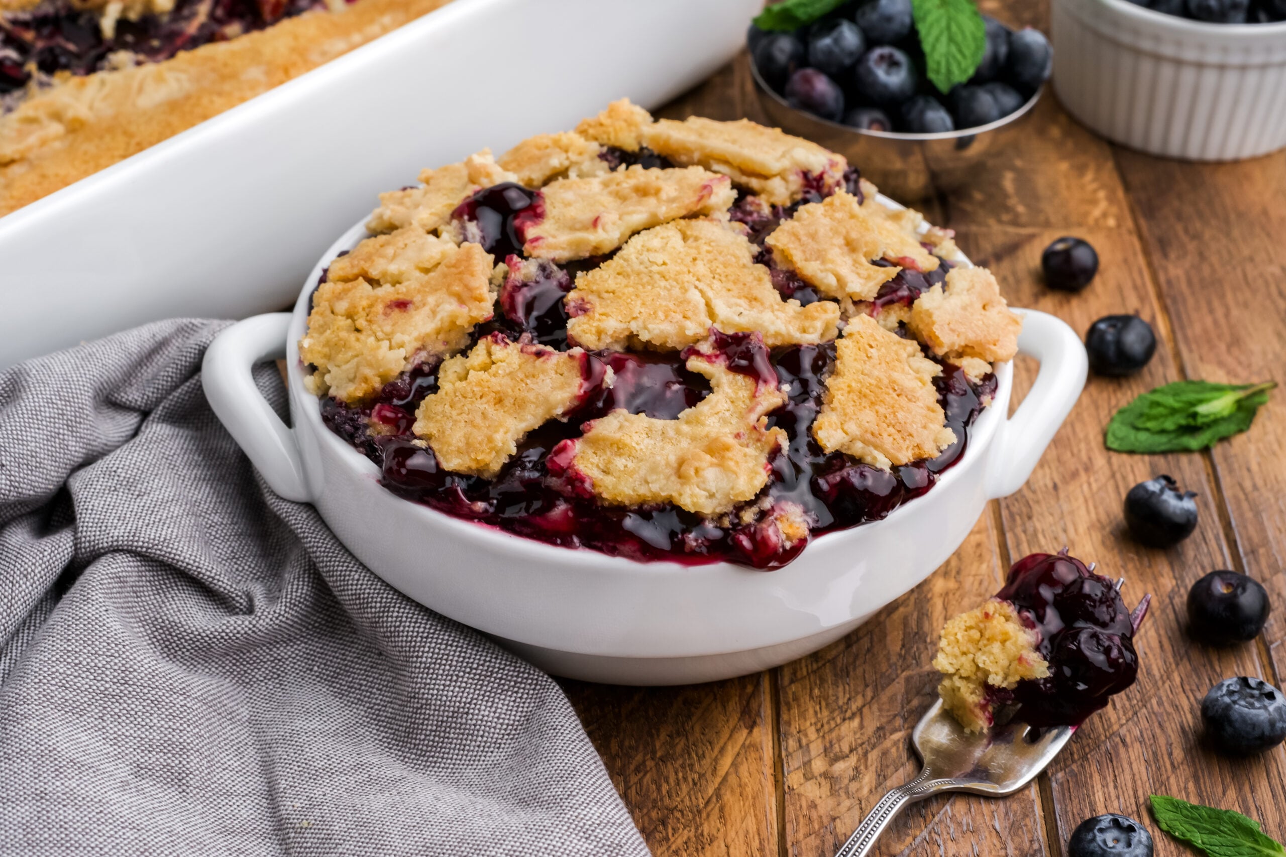 Blueberry Dump Cake in a white bowl on a dark wood table