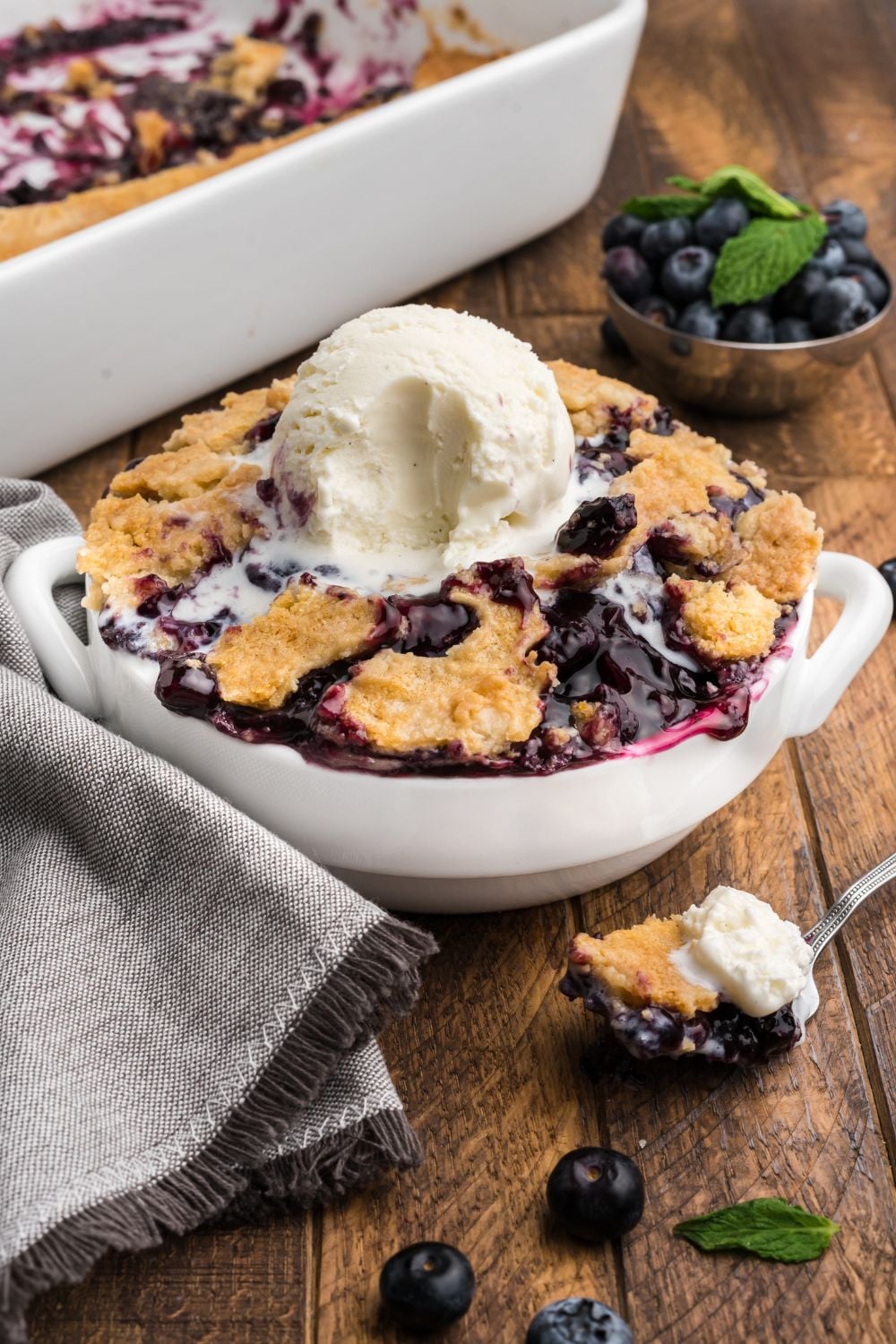 Blueberry Dump Cake in a white bowl, with ice cream in center with a bite taken out of it