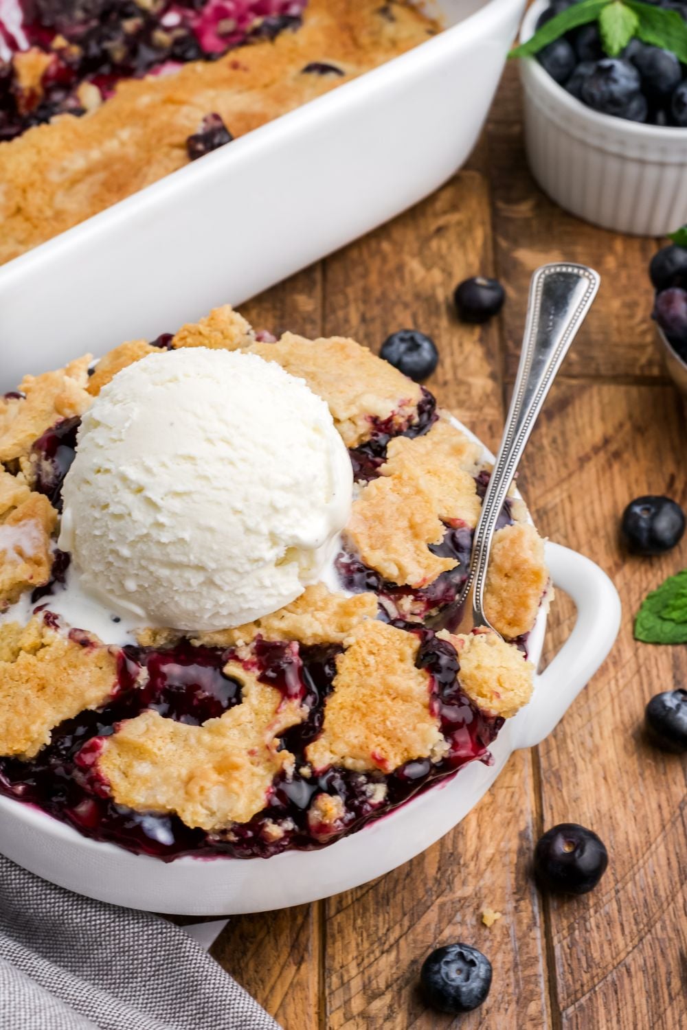 white bowl full of blueberry dump cake with a scoop of vanilla ice cream in the center