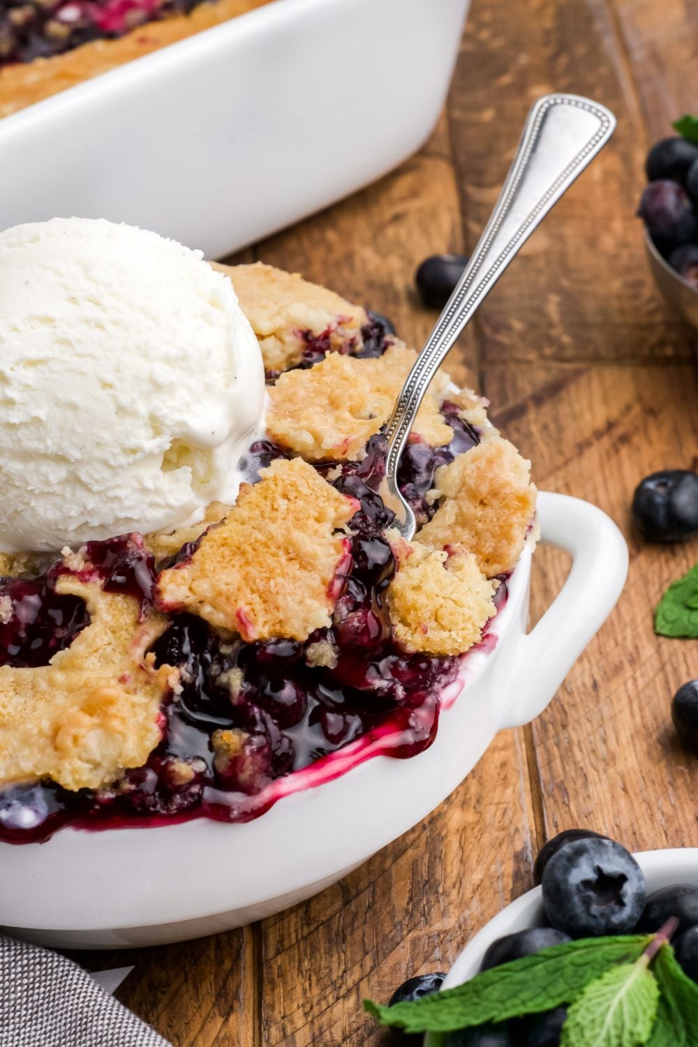 Blueberry Dump Cake in a bowl with a spoon dipping in it and a dollop of ice cream in the center of bowl