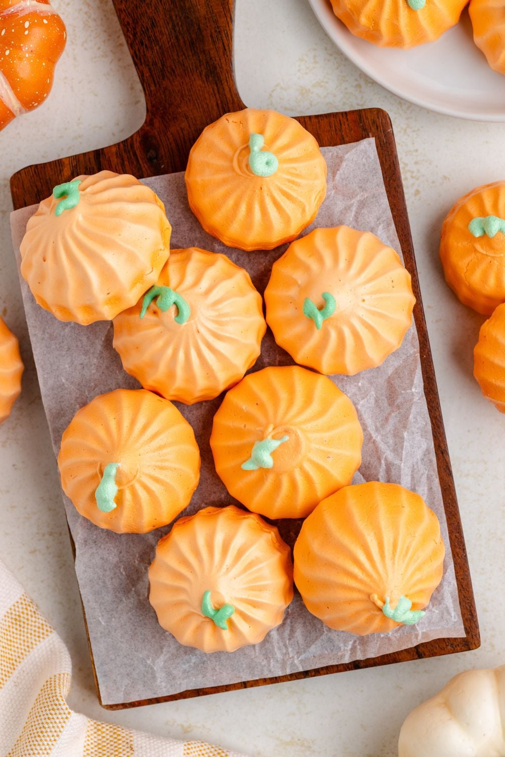 Crisp meringue cookies that look like pumpkins on a wooden tray and more on plates and placed on white table to give a fall themed look 
