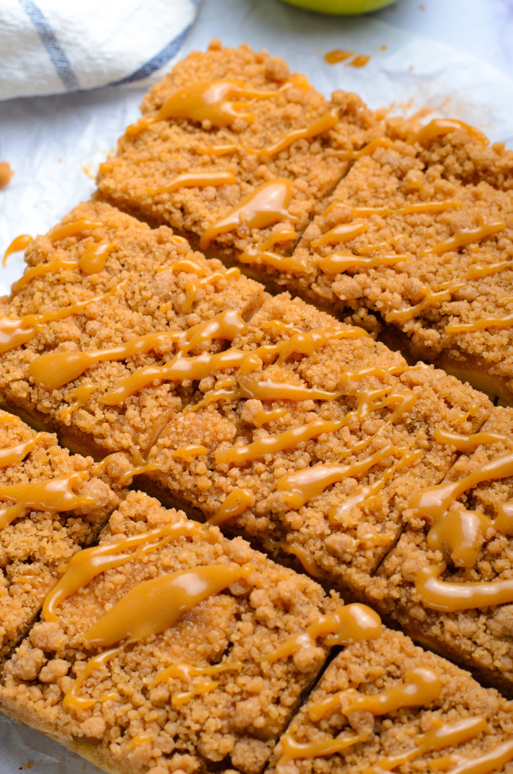 Up close shot of the Caramel Apple Pie Bars cut into squares with a drizzle of caramel sauce on top sitting on a table