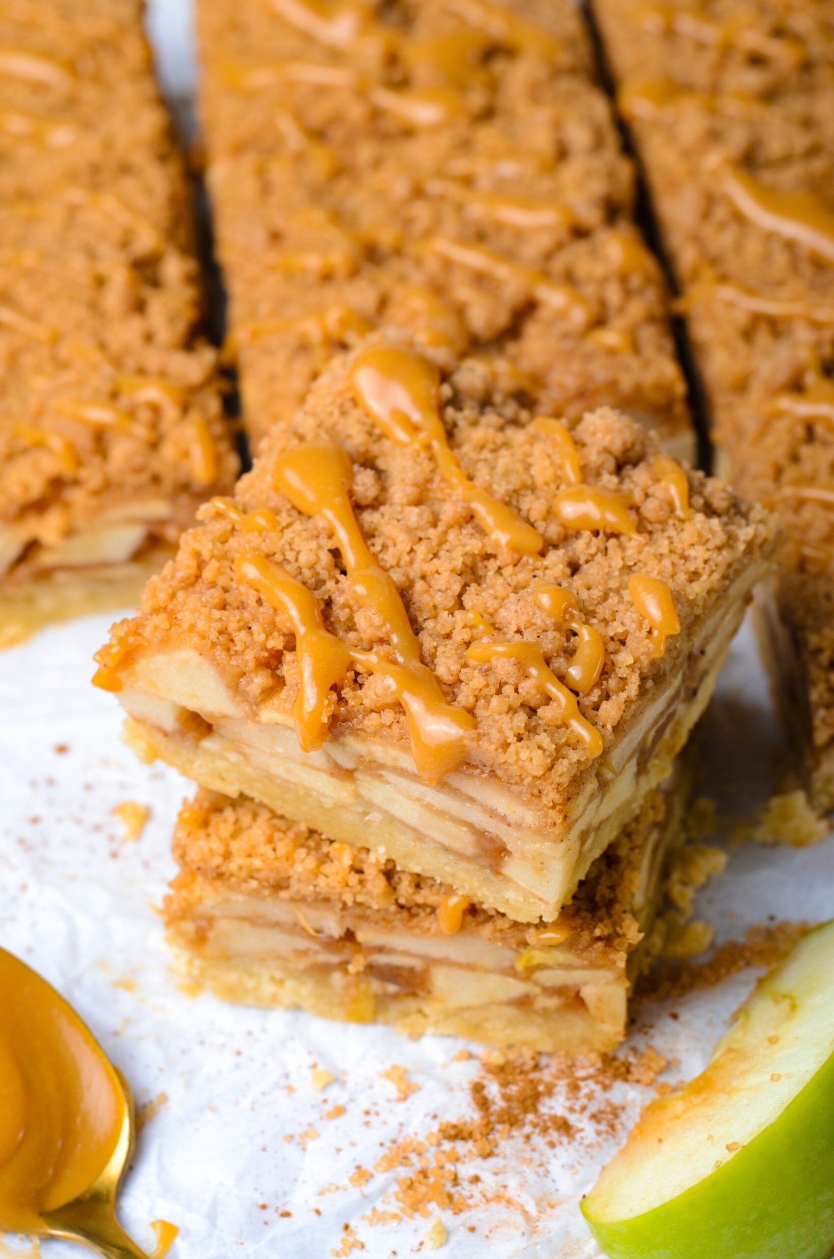 Caramel Apple Pie Bars stacked then placed on parchment paper showing apples in the center of the bars