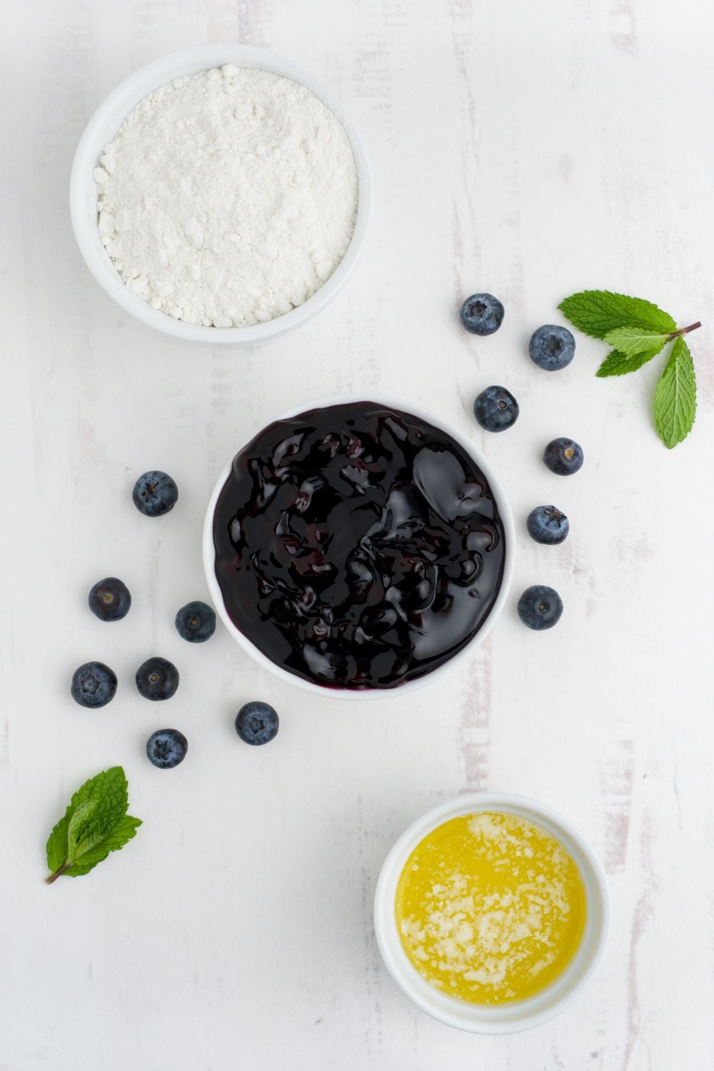 Blueberry Dump Cake ingredients in white bowls on a white table with fresh blueberries on table