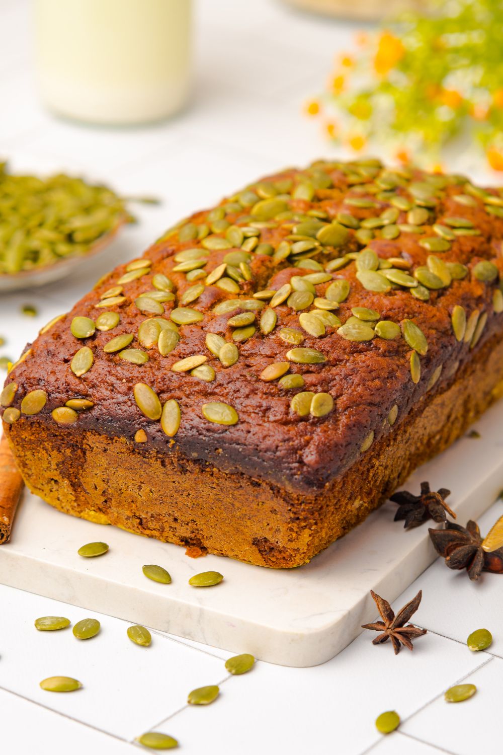 Starbucks Pumpkin Bread loaf sitting on a white marble cutting board on a white table. To the side is a bowl of seeds that is scattered around the table