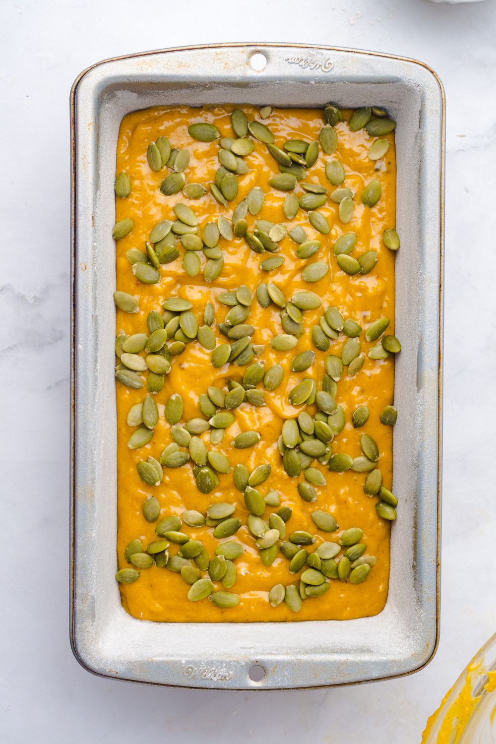 Starbucks Pumpkin Bread batter in a loaf pan on table topped with pumpkin seeds