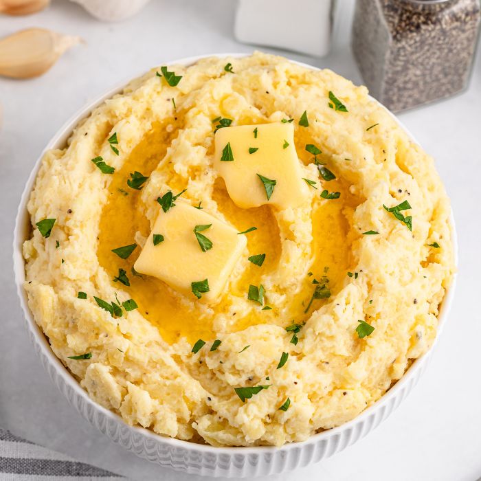 Garlic Mashed Potatoes in a white bowl sitting on a white table with salt and pepper shaker to the side of table