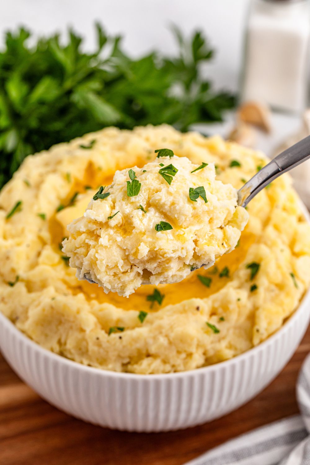 Garlic Mashed Potatoes with a spoon scooping up some out of the white bowl sitting on a wooden cutting board on the table
