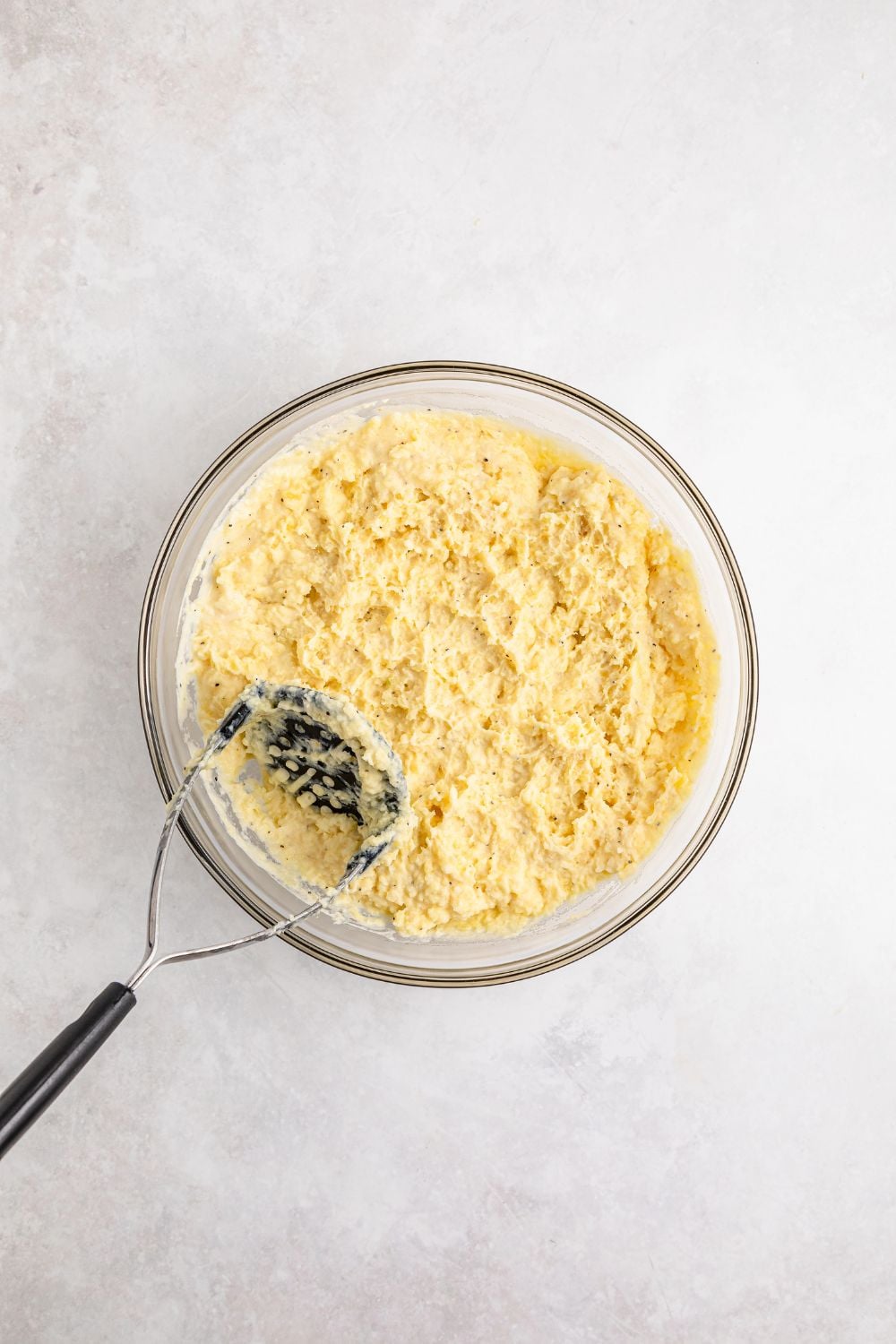 mashed potatoes in a glass bowl with a potato masher placed in the bowl
