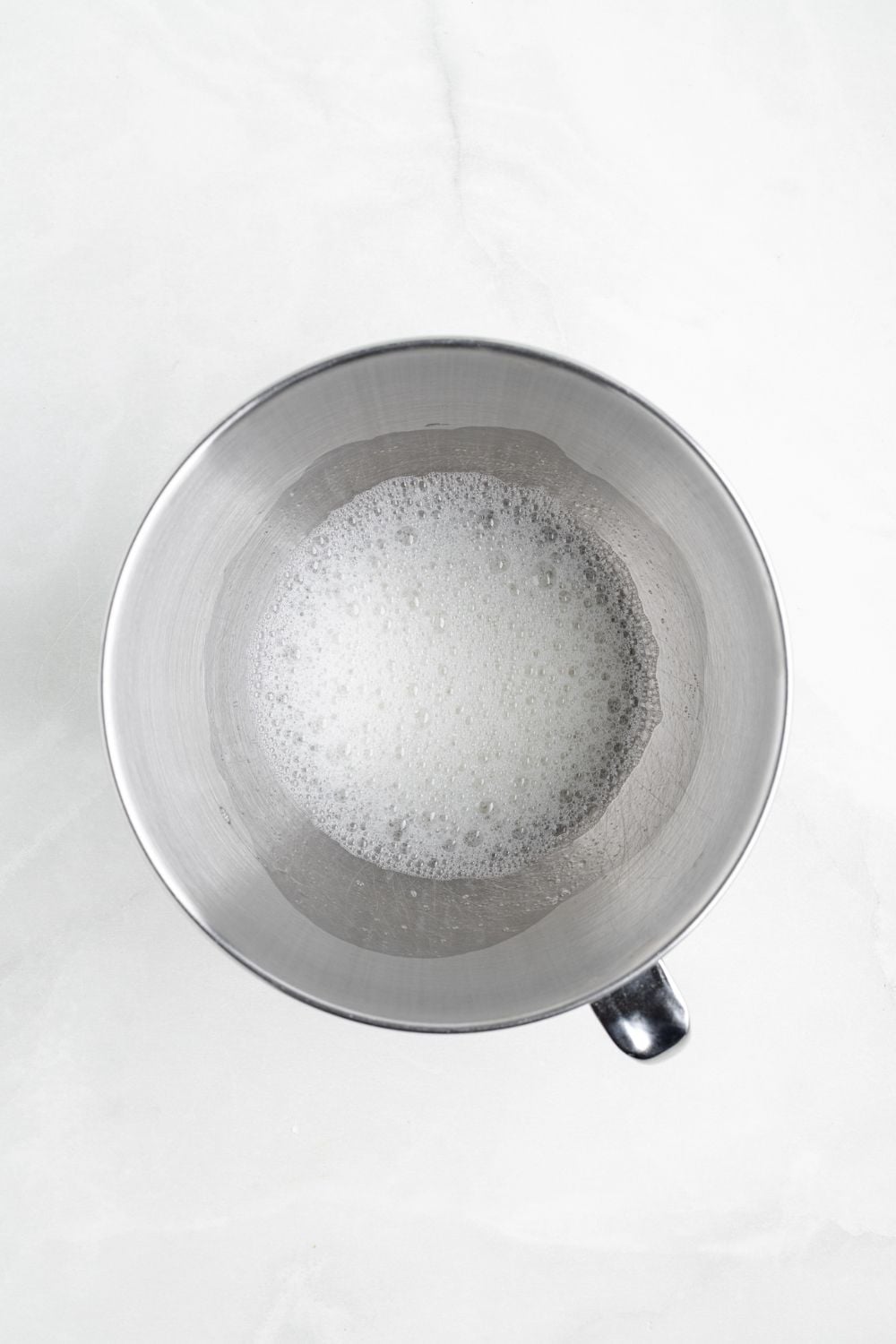 egg whites in a metal mixing bowl on a white counter 