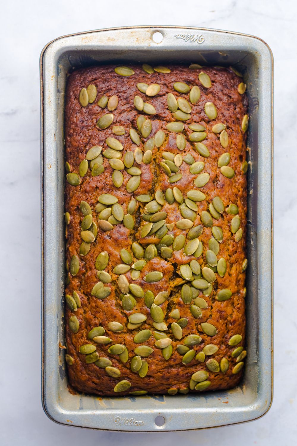 Starbucks Pumpkin Bread in a loaf pan on table with pumpkin seeds all over the top of bread