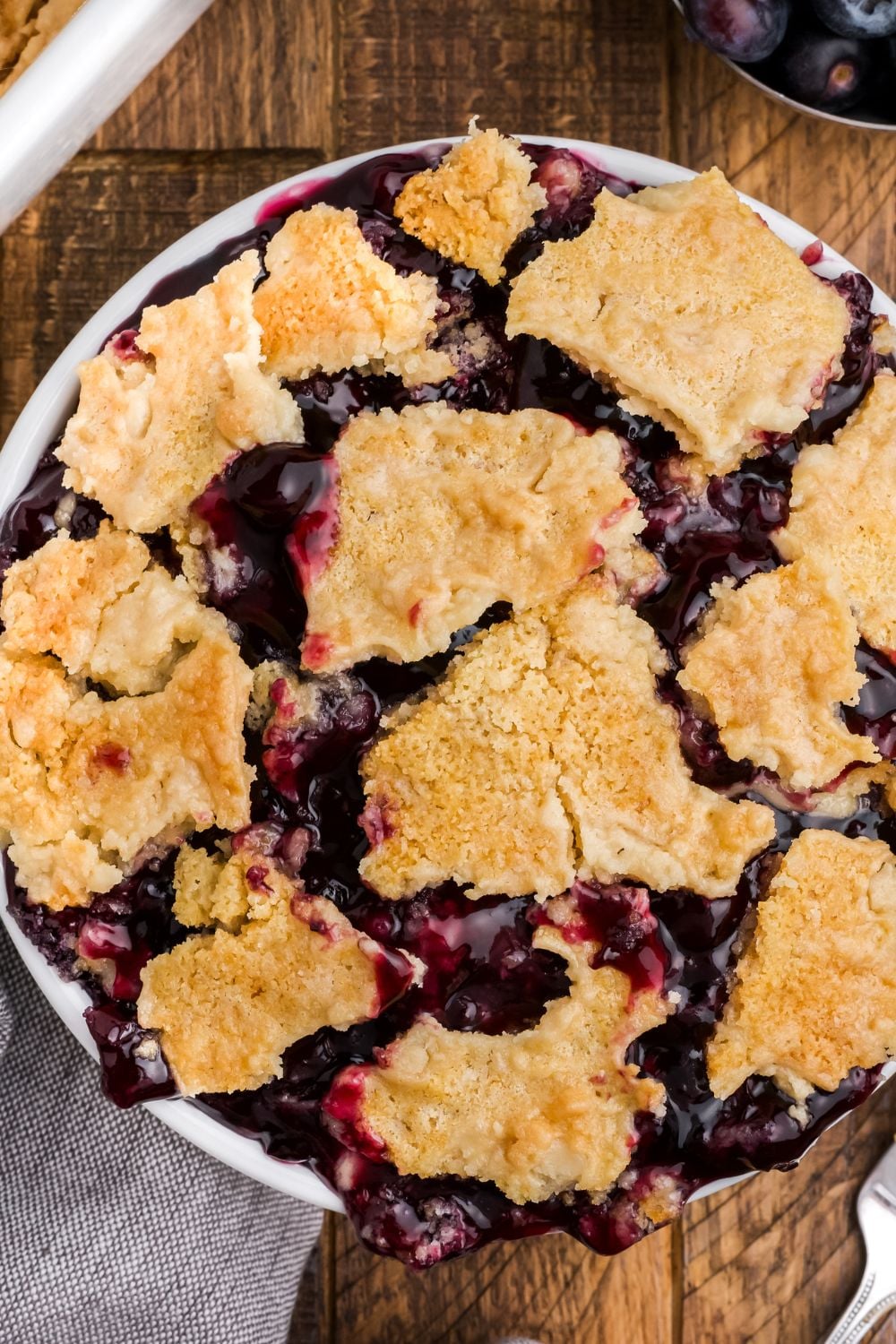 close up of Blueberry Dump Cake in a white bowl on table on a wooden table
