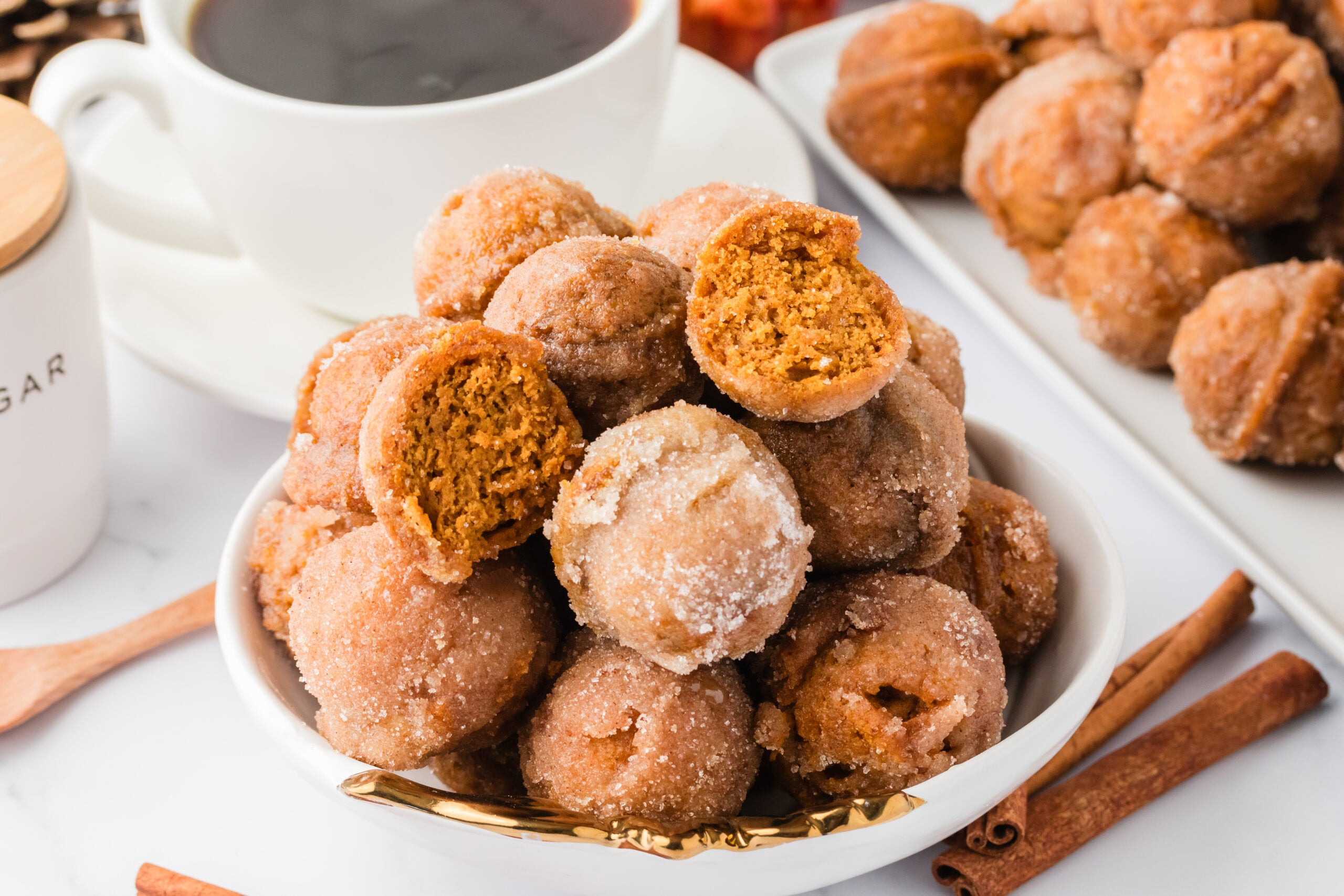 Pumpkin Spice Donut Holes on a white plate with a cup of coffee in the background