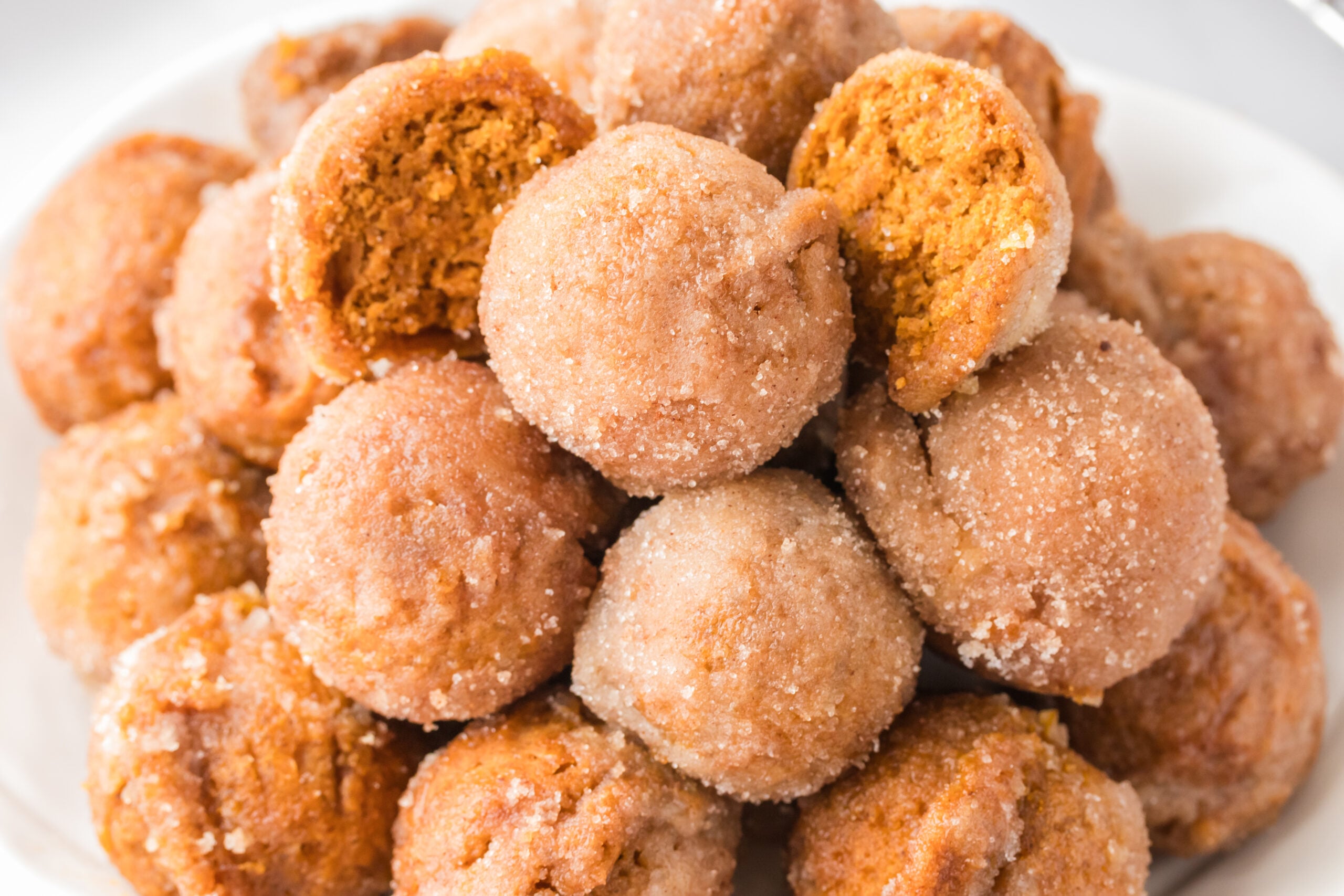 Pile of Pumpkin Spice Donut Holes on a white plate with one cut open to see the inside 