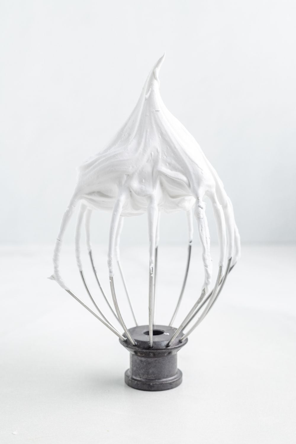 a whisk sitting on table with stiff meringue on it 