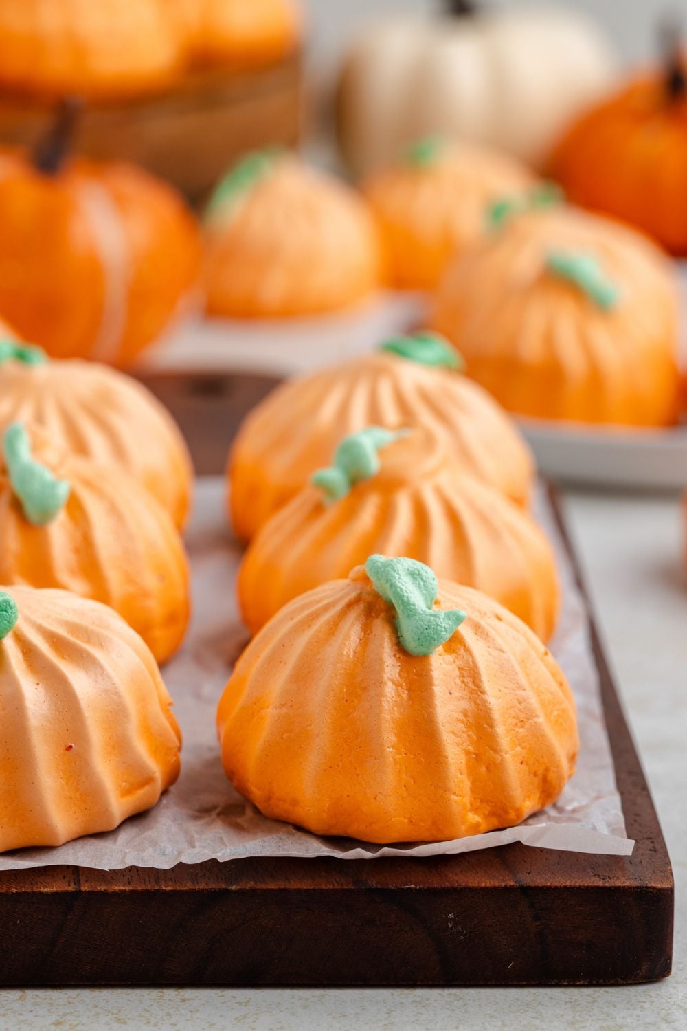 side view of table with a wooden tray with Pumpkin Meringues placed in single rows and more cookies behind it on table 