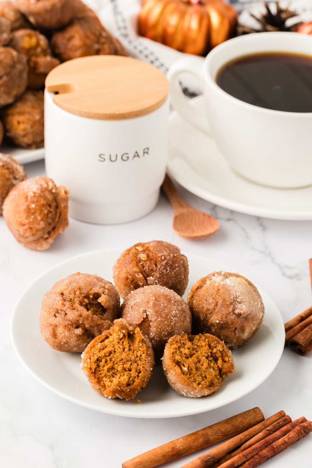 plate with pumpkin spice donut holes and some are cut in half. A cup of coffee, cinnamon sticks andmore around table