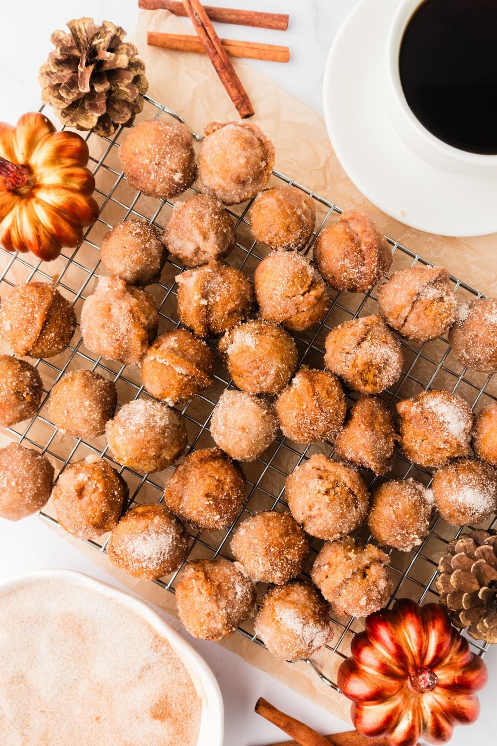 Pumpkin Spice Donut Holes scattered on a cooling rack on table with a faux pumpkin to side 