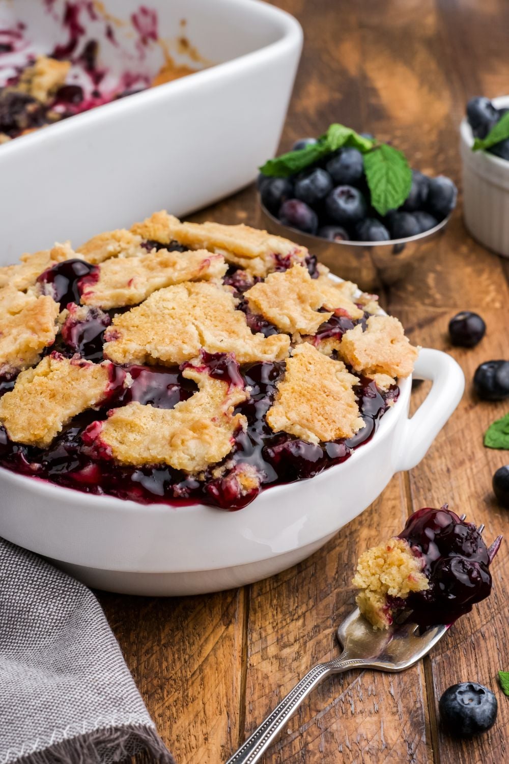 Blueberry Dump Cake in a white bowl on wooden table with blueberry and cake
