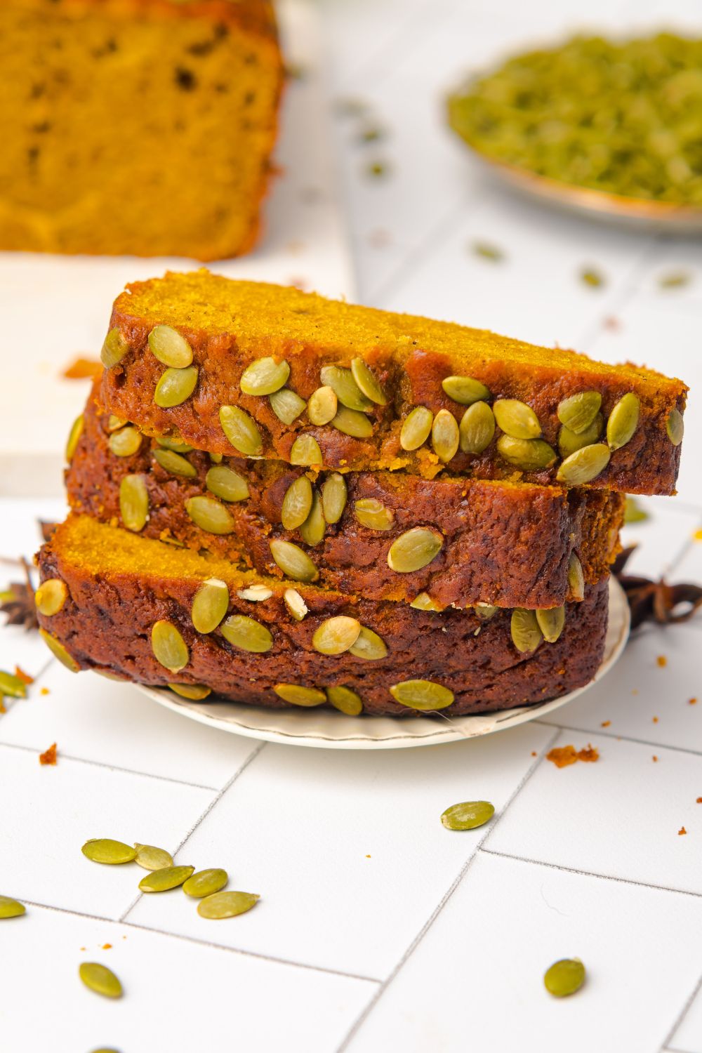 Starbucks Pumpkin Bread stacked on a plate with pumpkin seeds on top of bread and in a bowl to the side
