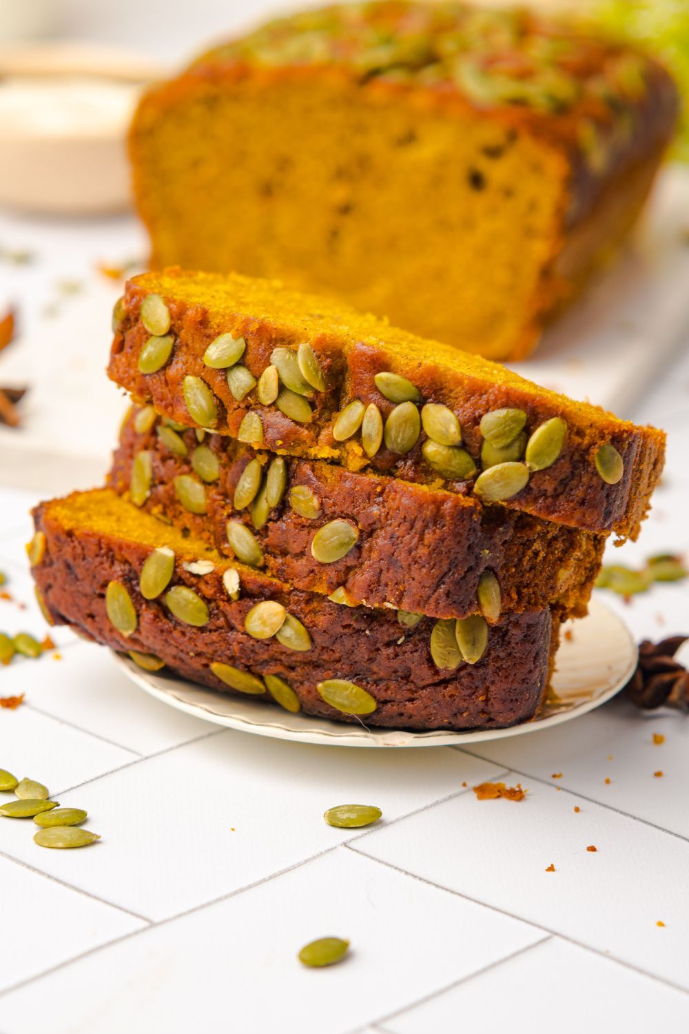 small white plate with a stack of Starbucks Pumpkin Bread on it, and the rest of the loaf behind it on table