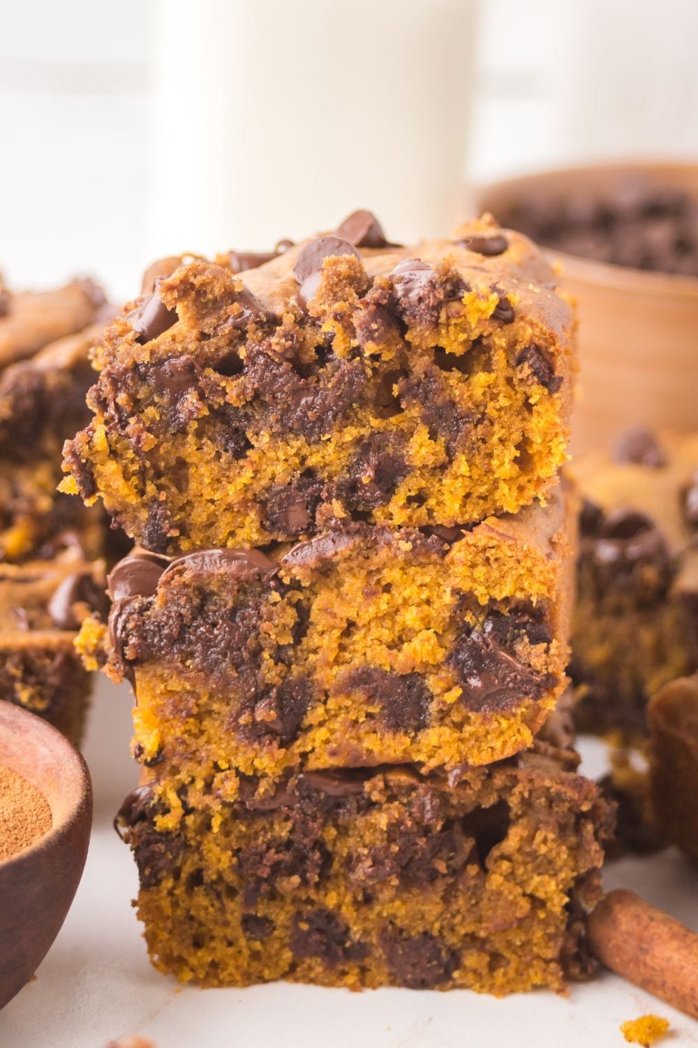 sliced squares of Brown Butter Pumpkin Chocolate Chip Bars stacked on top of one another on white table with more bars around the table