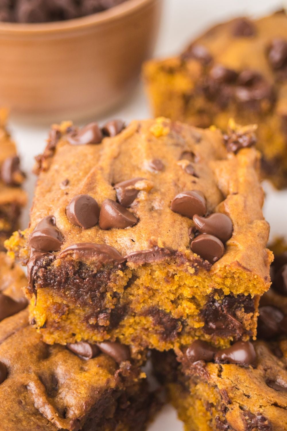 Brown Butter Pumpkin Chocolate Chip Bars stacked on top of one another on a white platter sitting on the table