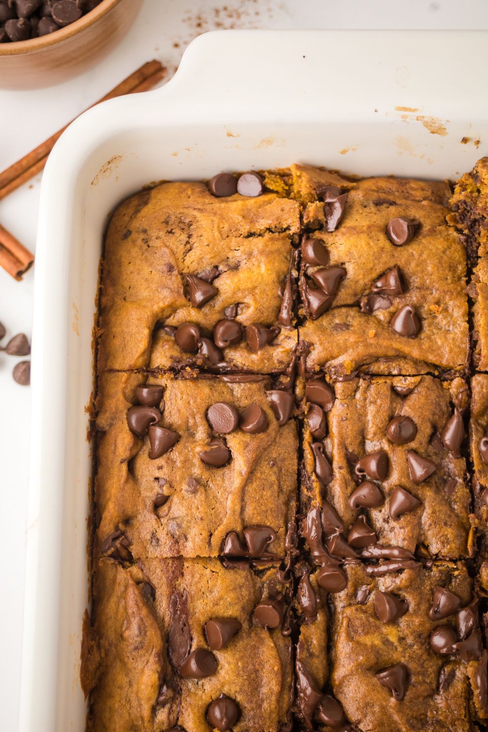 view of a portion of a white casserole pan full of Brown Butter Pumpkin Chocolate Chip Bars on a white table