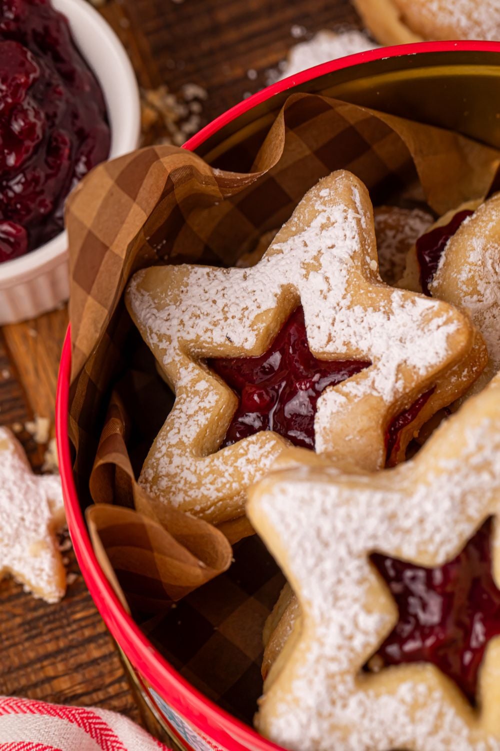 Linzer cookies in a red tin on table with a small bowl of jam