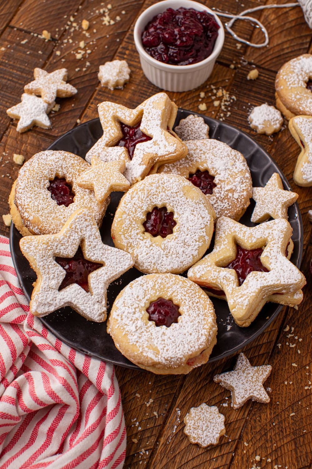 a wooden table with a plate of Linzer cookies and more scattered around the table