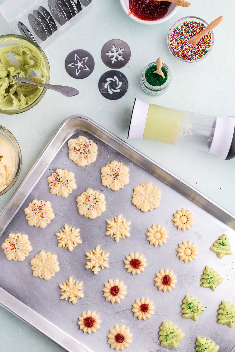 raw Spritz Christmas Cookies on a sheet pan with more cookie dough around the table