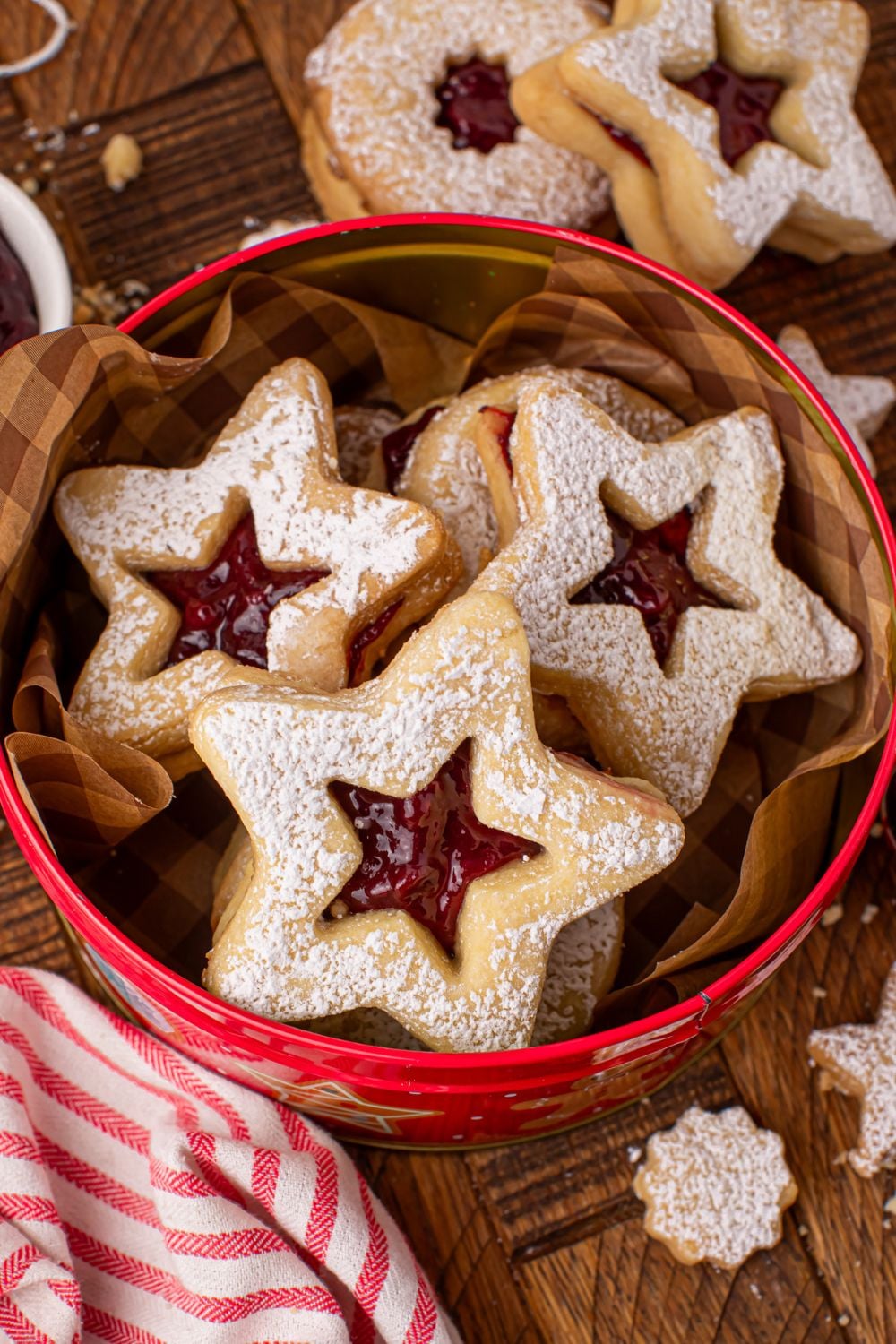Cutout Linzer cookies in a red tin on a table with a towel in front