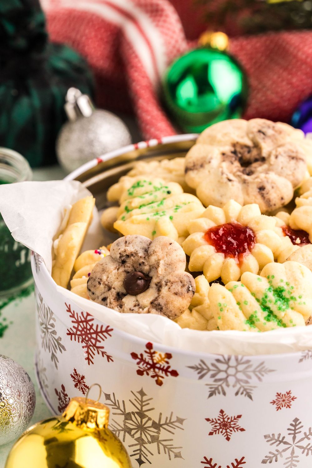 a metal bowl full of a mix of Christmas spritz cookies with Christmas ornaments around the table