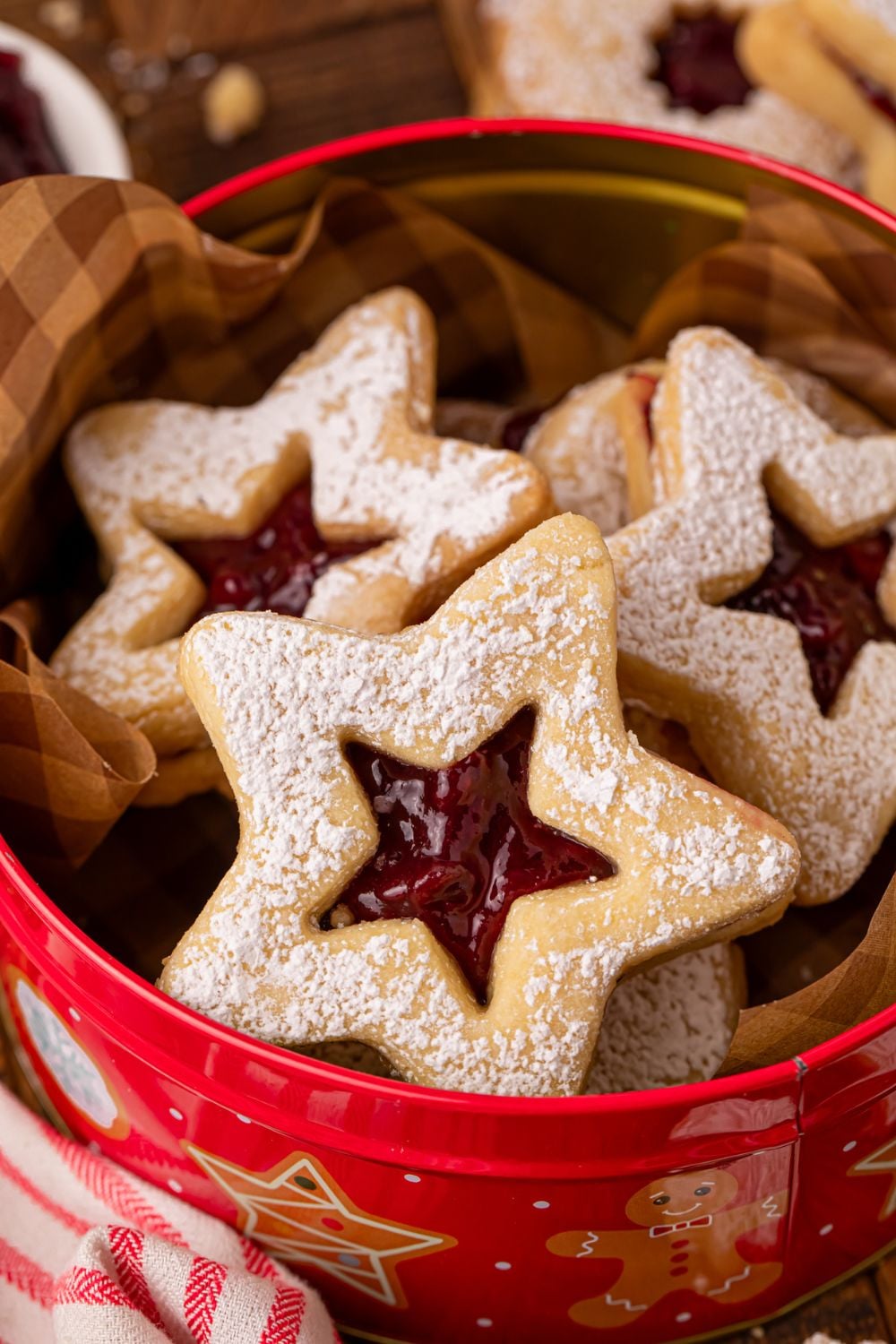 Linzer cookies in a tin with a towel to side on wooden table