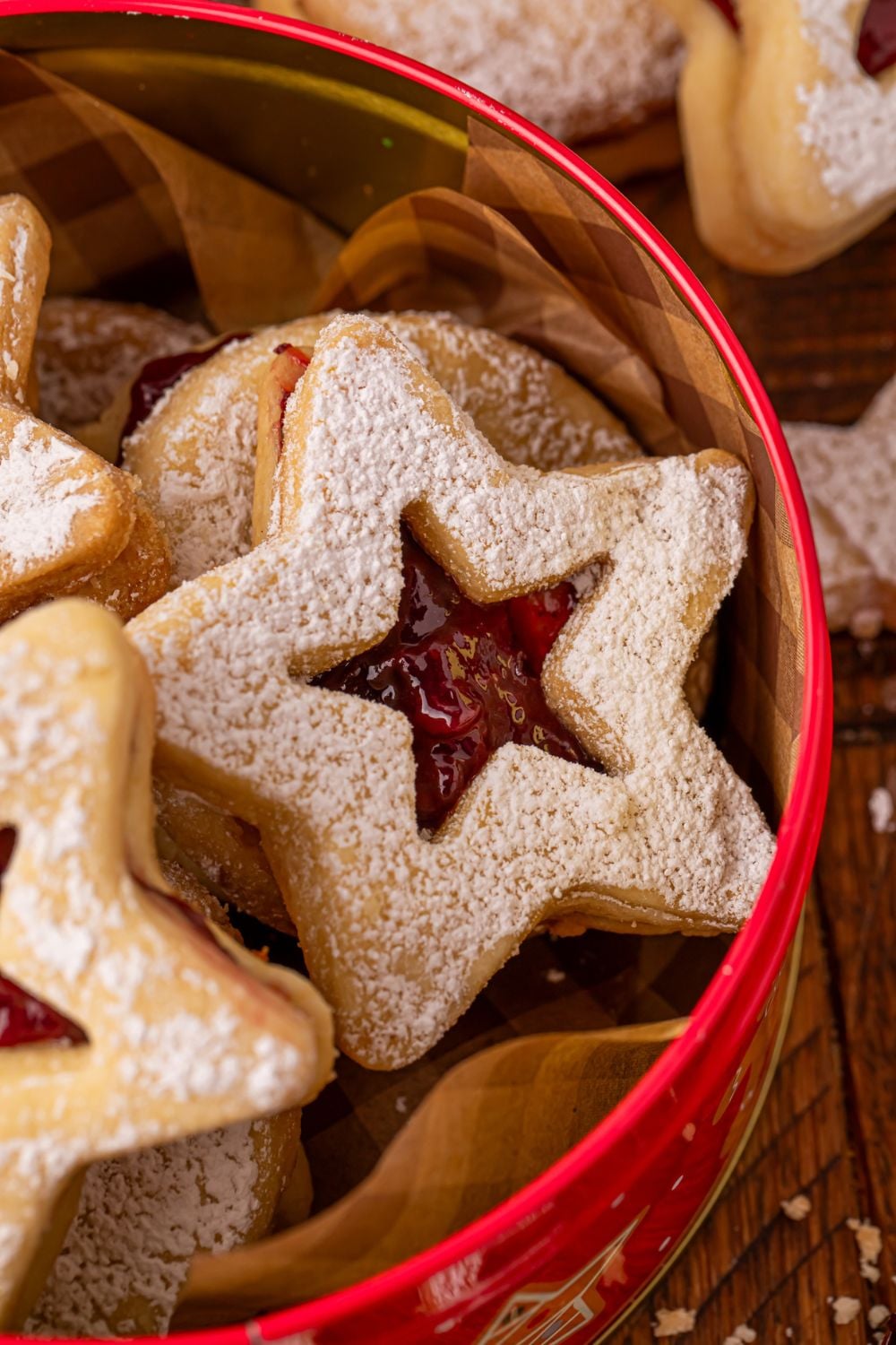 close up look of jam filled linzer cookies in a metal tin on table