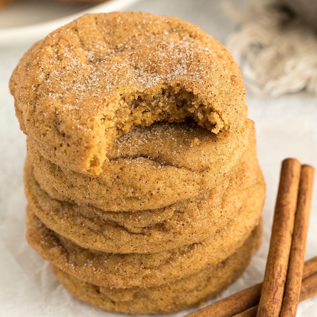 Pumpkin Snickerdoodle Cookies stacked on top of one another on table with a bite taken out of the top one 